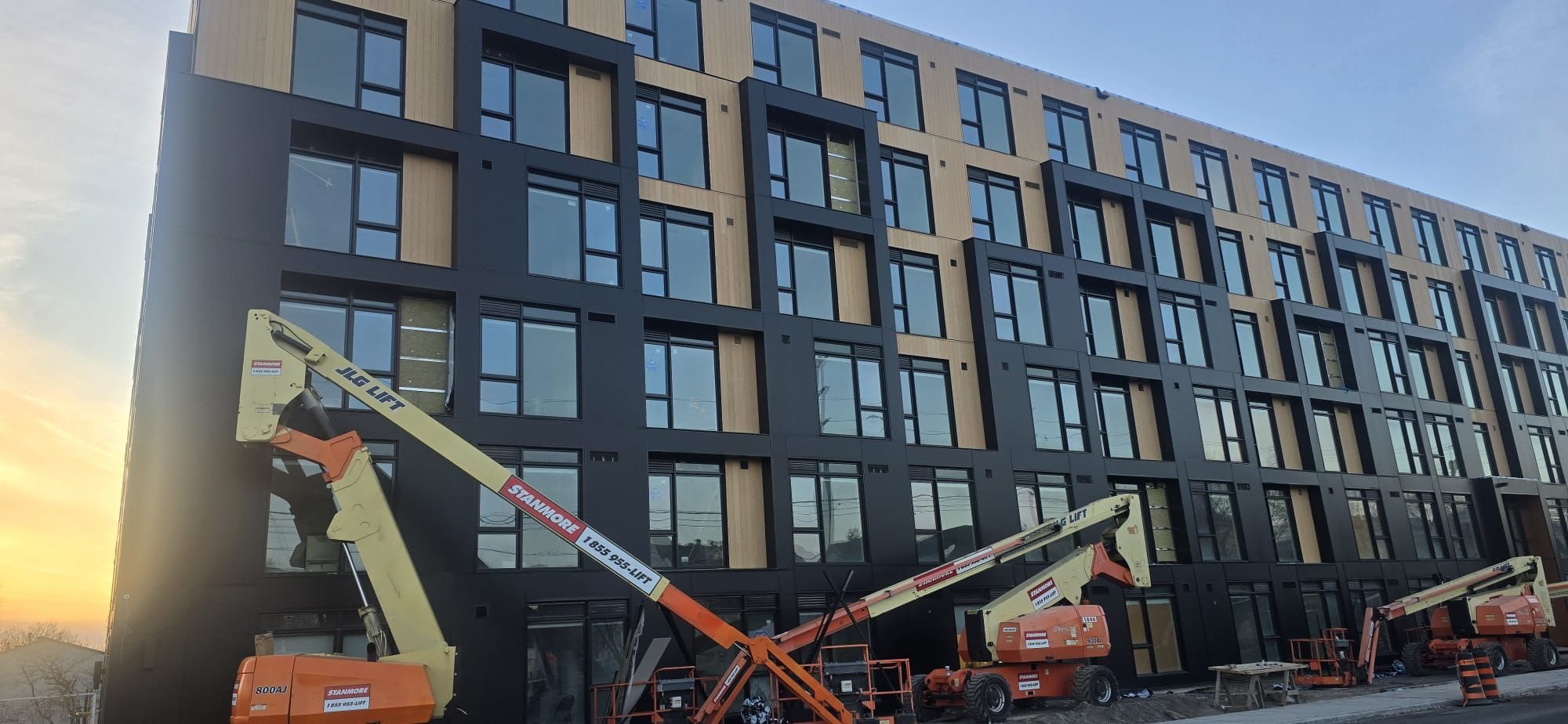 Multi-family building with black metal and wood-look cladding installed by Toronto Siding Pro at sunset